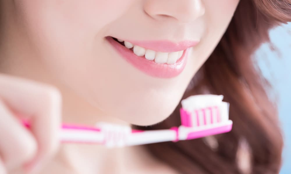 歯磨き粉が乗ったピンク色の歯ブラシを口元に寄せて微笑んでいる女性の画像