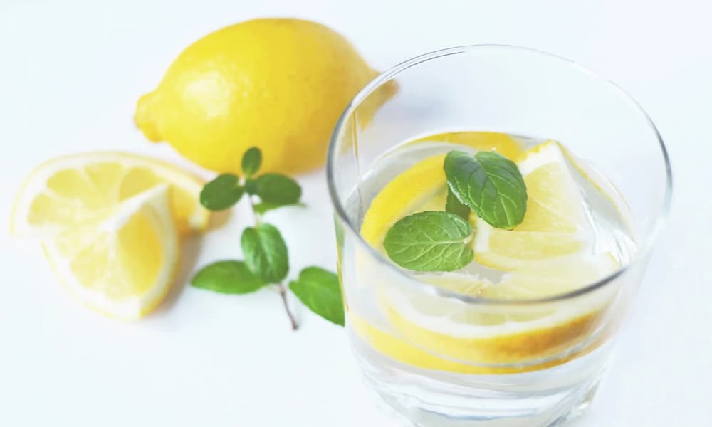 輪切りレモンを浮かべたレモン水が入っているグラスとレモンの画像