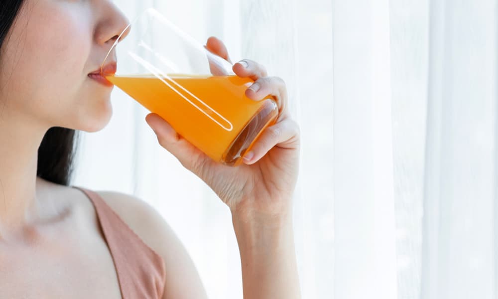 グラスに入ったオレンジ色の飲み物を飲む女性の画像