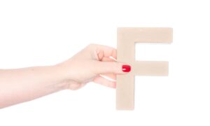 「F」の茶色いブロックを持った女性の手の画像