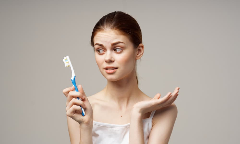 右手に歯ブラシを持ちながらそっぽ向いている女性の画像