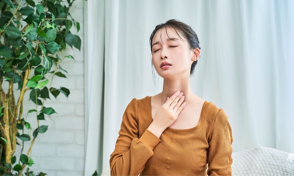 のどに手を添えて目を閉じている若い女性