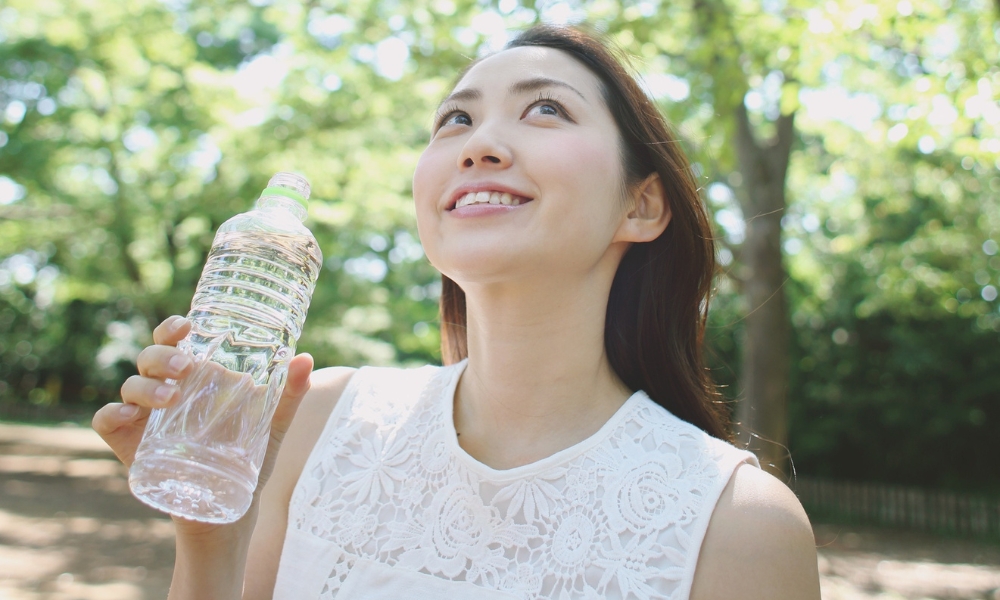 水の入ったペットボトルを持ちながら自然の空気を感じている若い女性