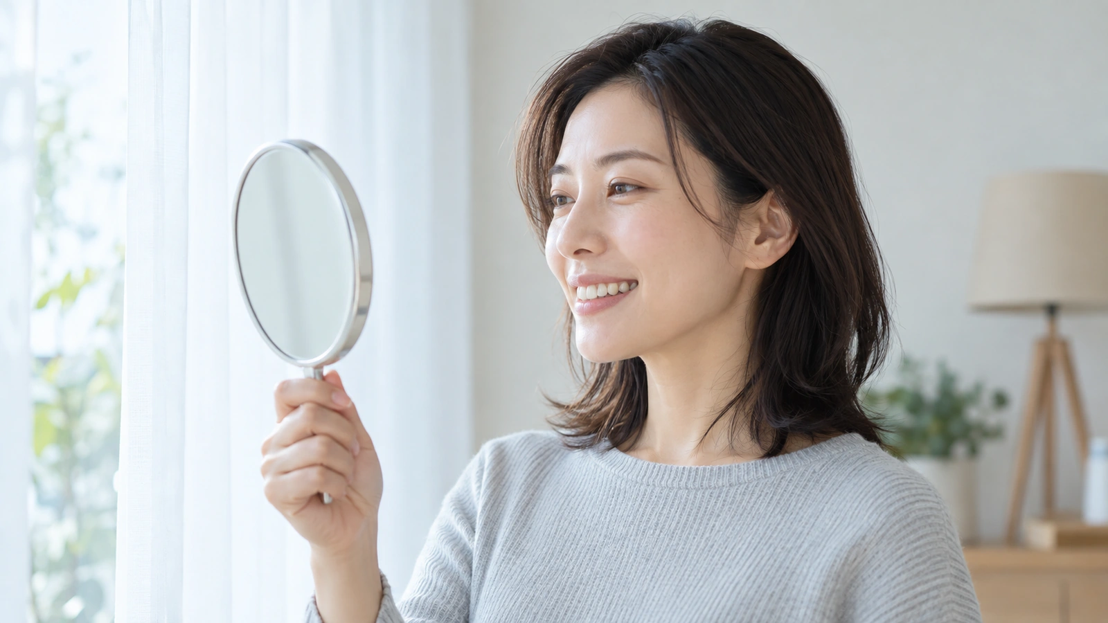 窓からの柔らかな光の下で手鏡を使い口元を確認する女性