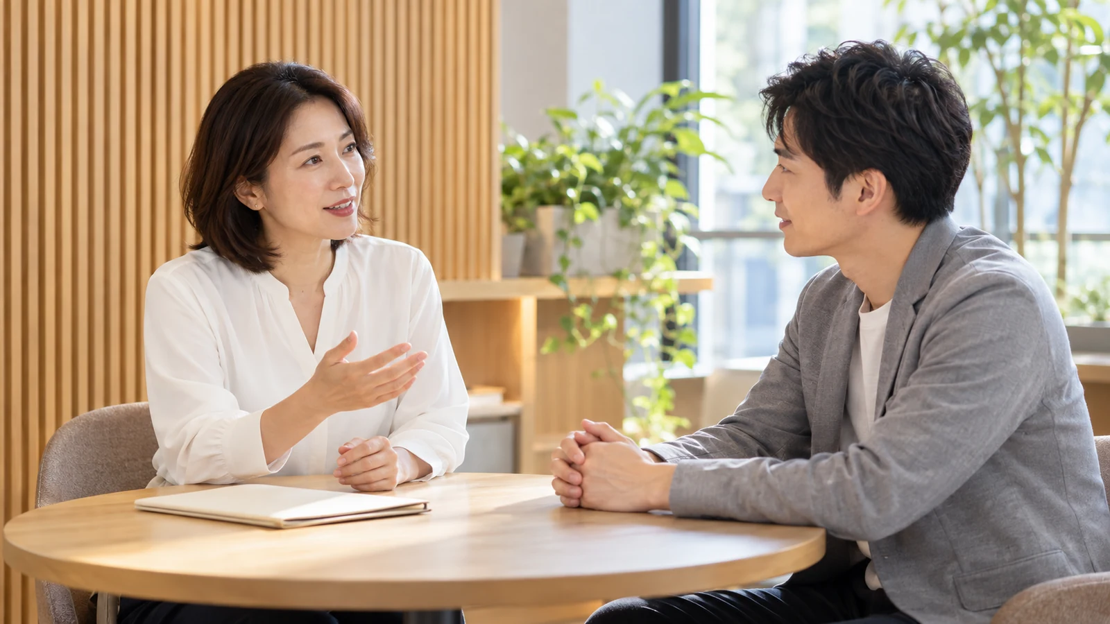 丸テーブルを囲み、落ち着いて話し合う二人のビジネスパーソン