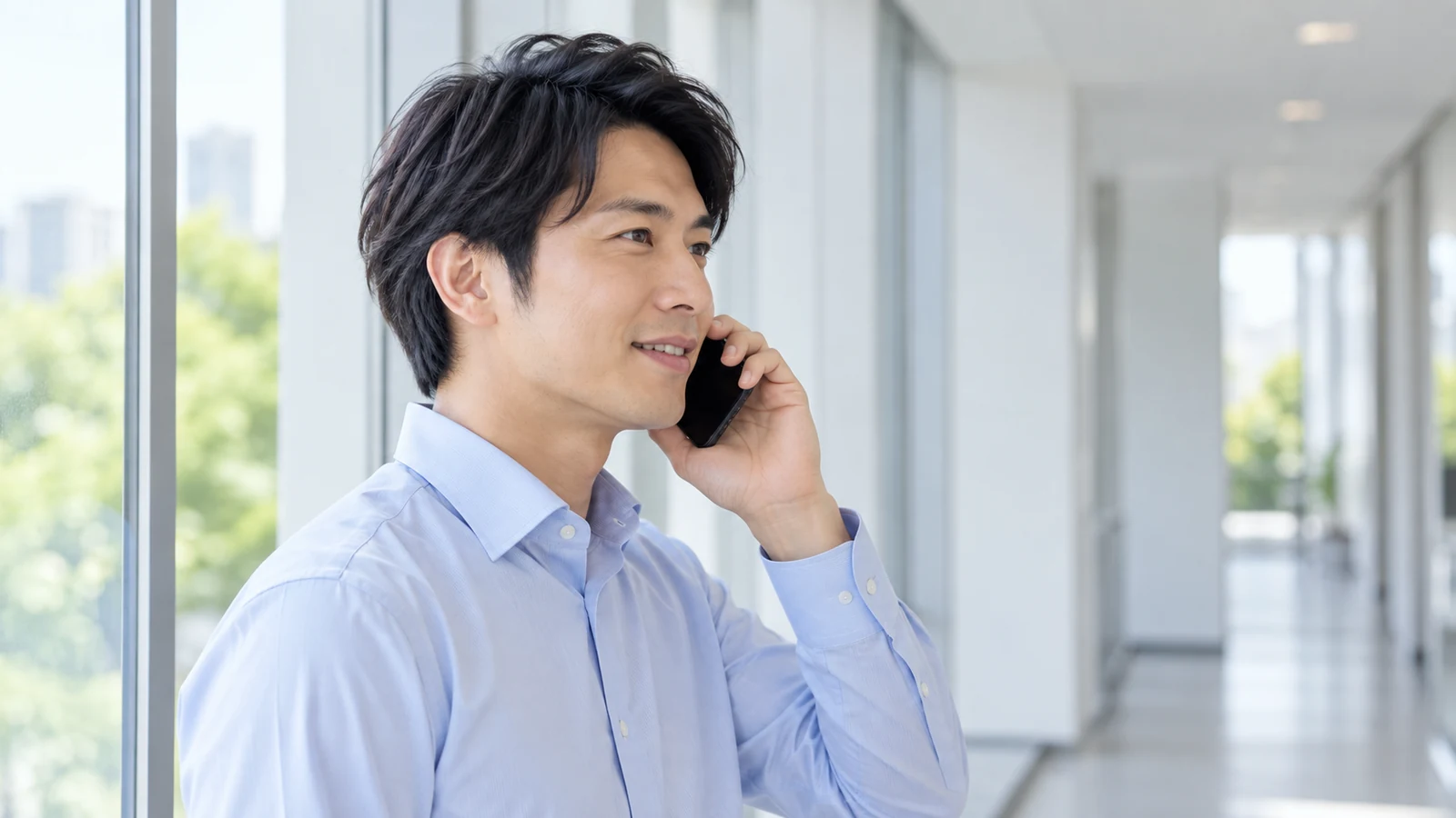 窓辺で相手の話を聞きながら電話に応対する男性