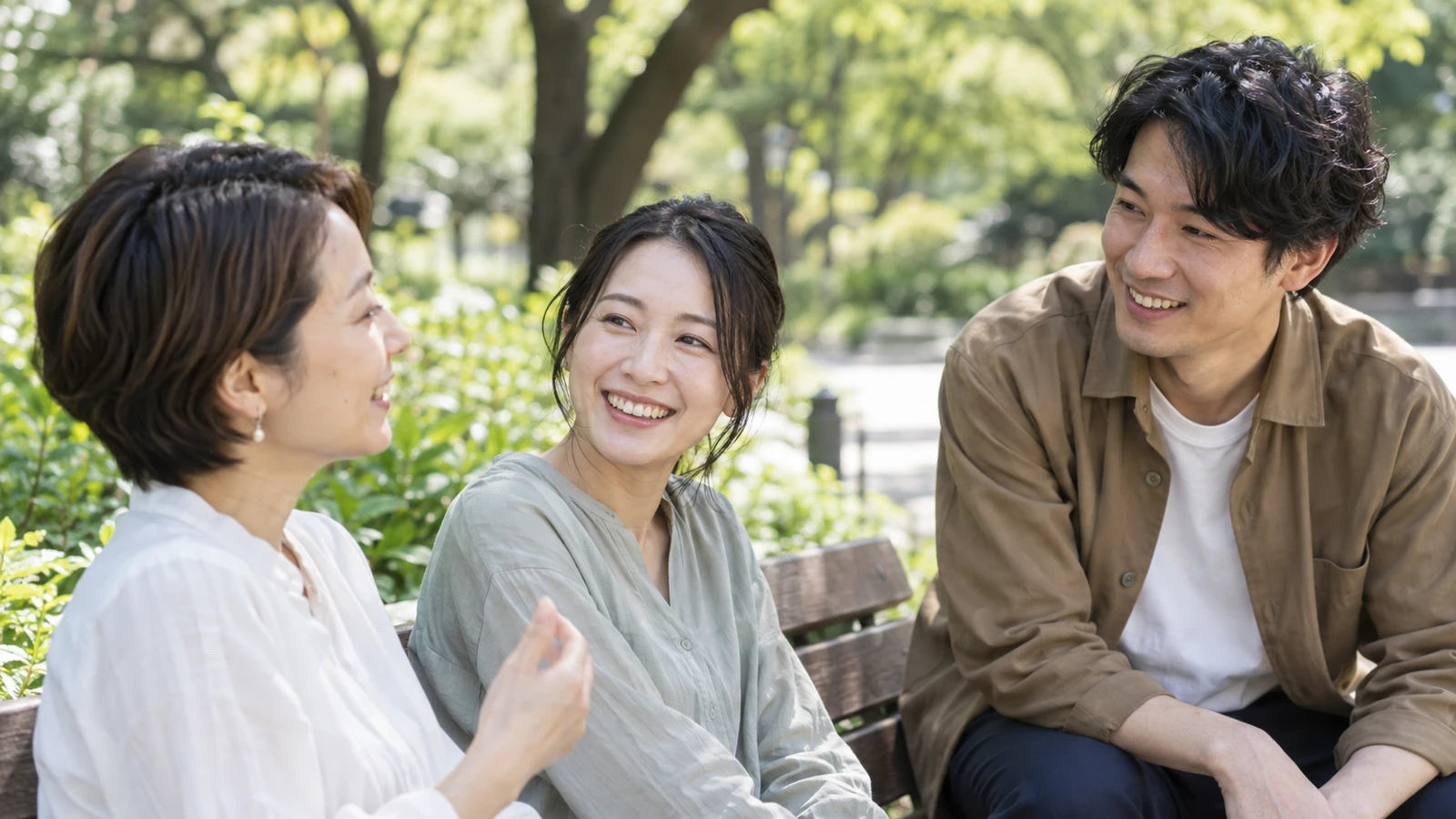 緑のある公園のベンチで自然に会話する3人の成人